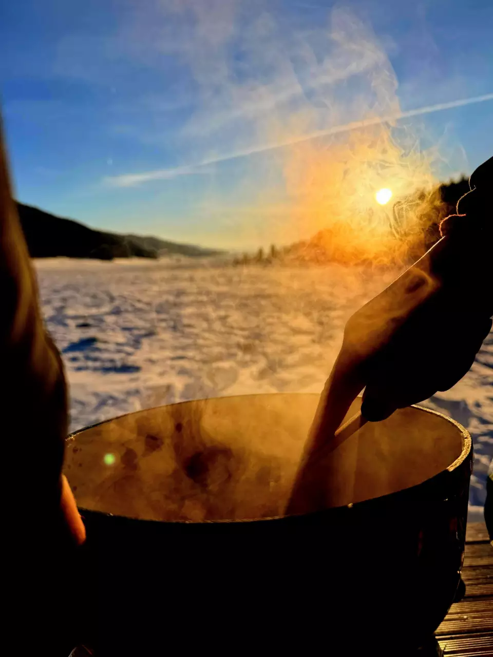 Mains au-dessus d’un récipient fumant en plein paysage enneigé.