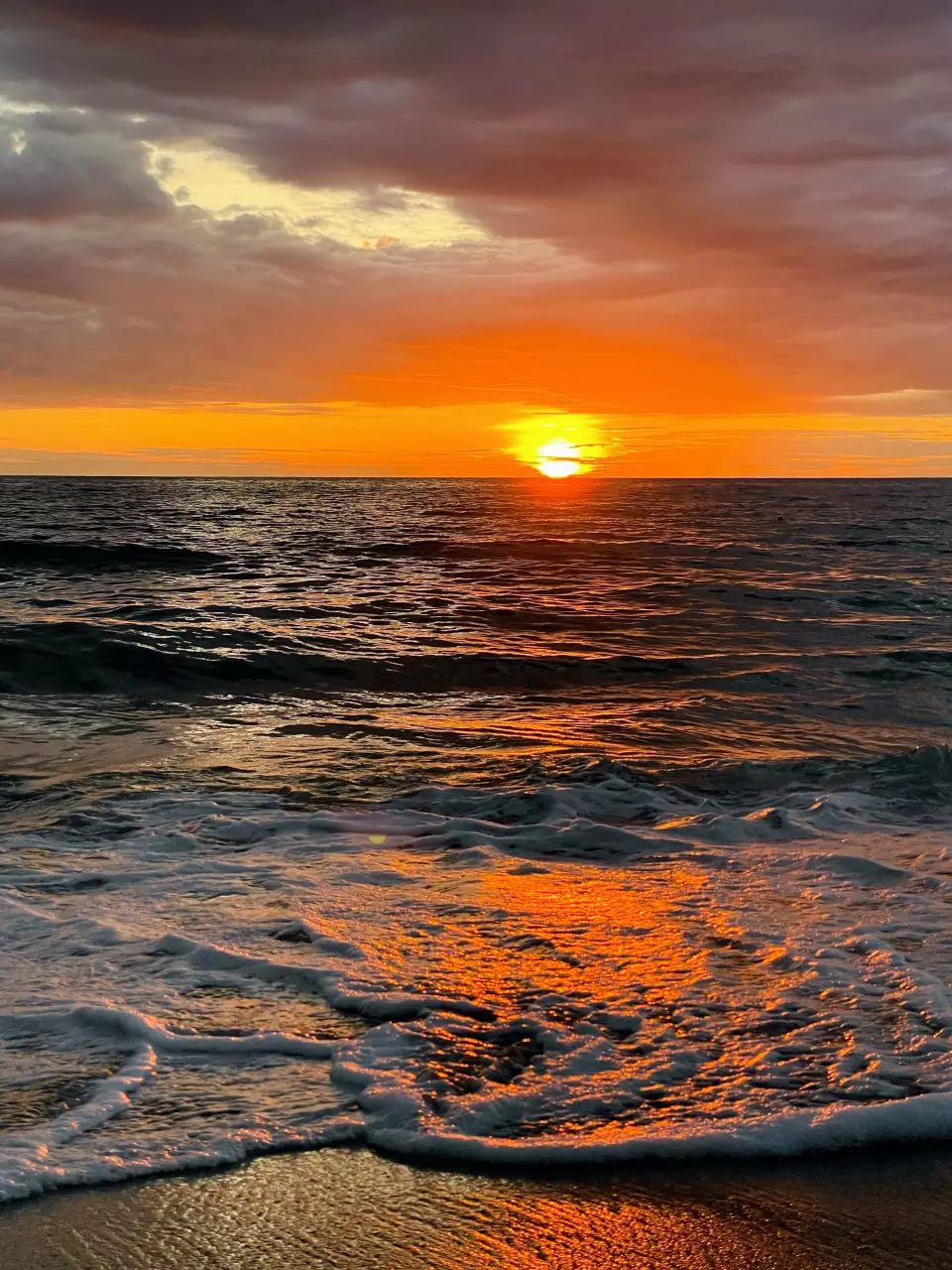 Coucher de soleil orange sur l’océan avec une vague qui arrive sur la plage.