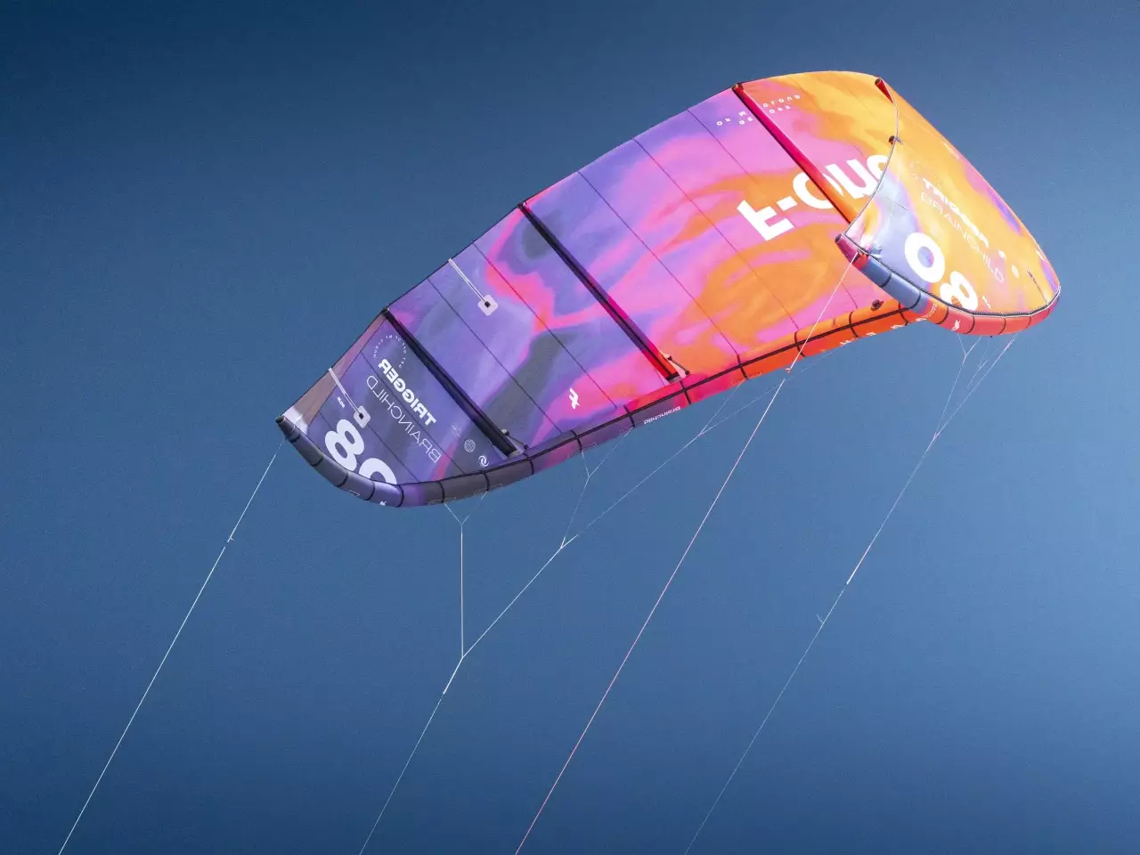 Aile F-ONE Trigger v2 orange et violette en gros plan sur un ciel bleu profond.